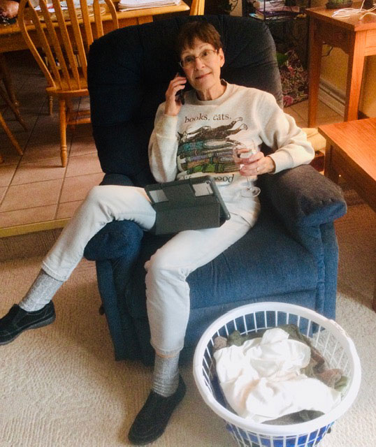 woman in a chair holding a class of wine, phone and tablet