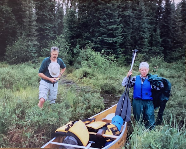 2 people stading near canoe with camping gear