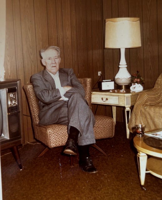 man in a suit sitting on orange chair near a table with a lamp